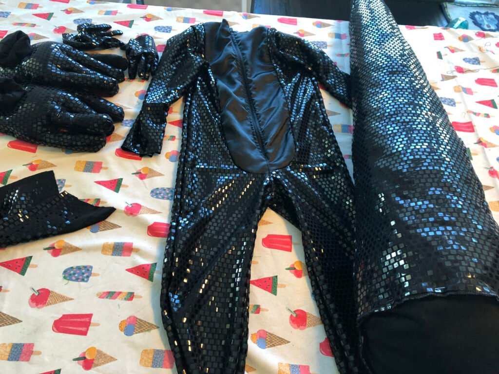 Handmade salamander costume pieces laid out: body suit, gloves and tail in black sequined fabric