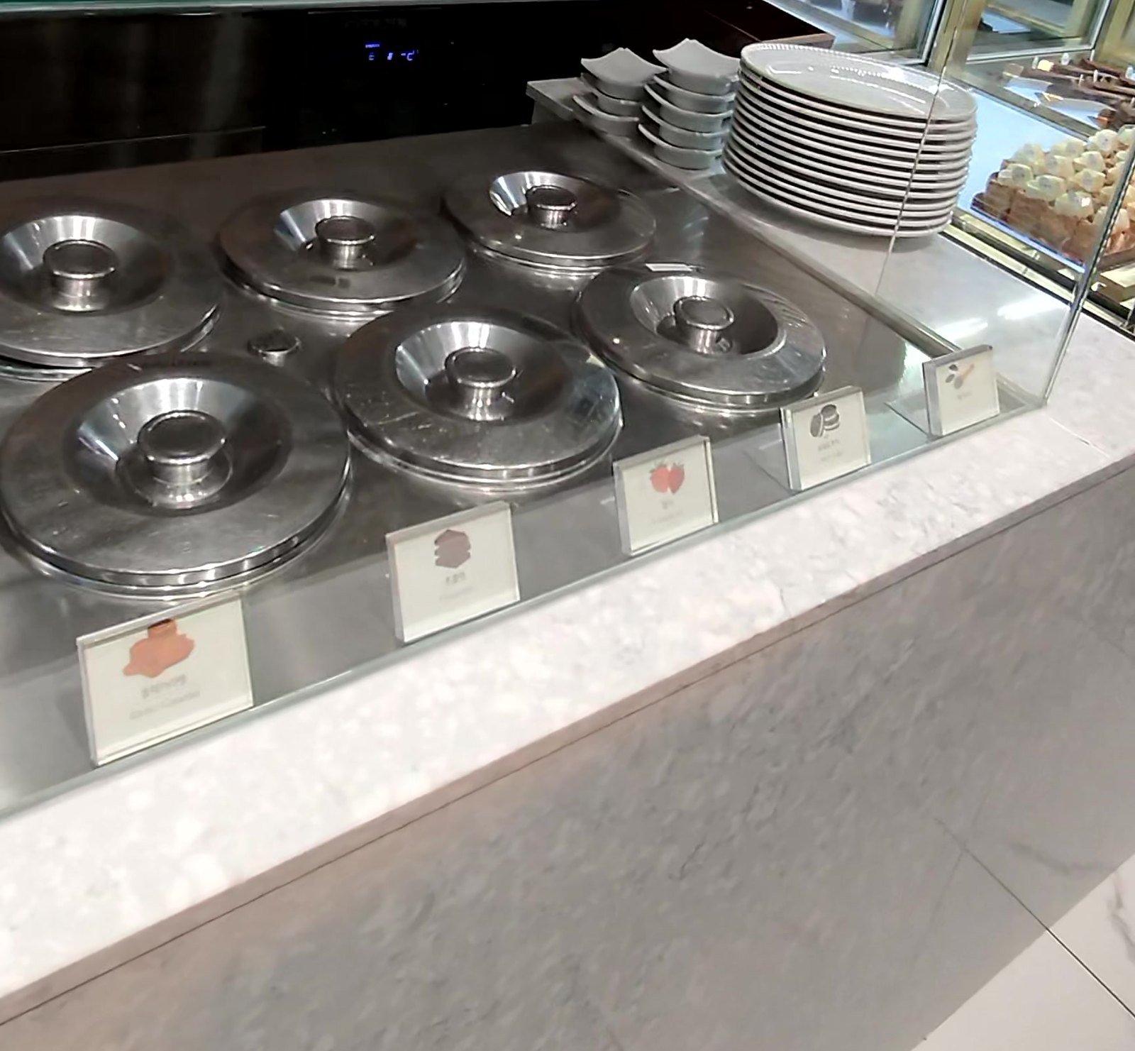 Row of covered gelato tubs and stacked plates at the dessert corner of Crab 52 Seoul