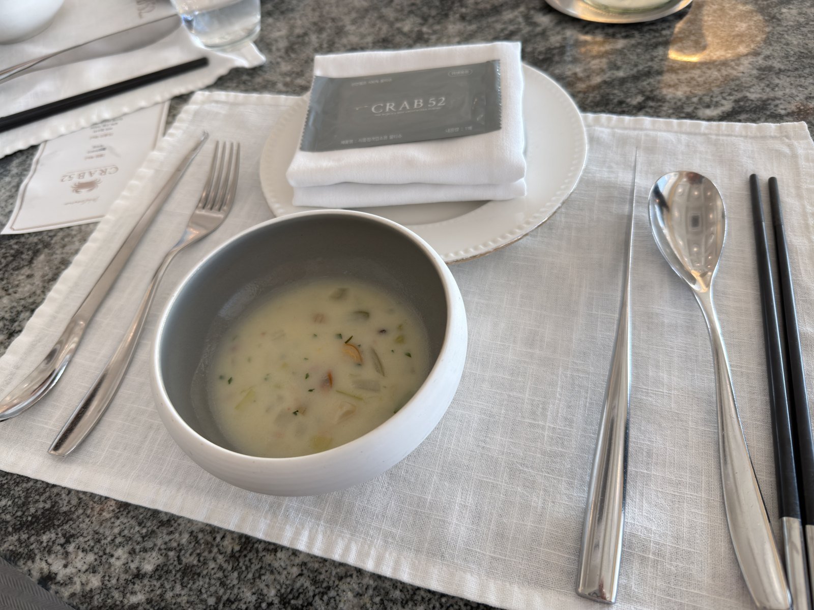 Crab 52 branded napkin, cutlery and the welcome clam chowder on a marble table