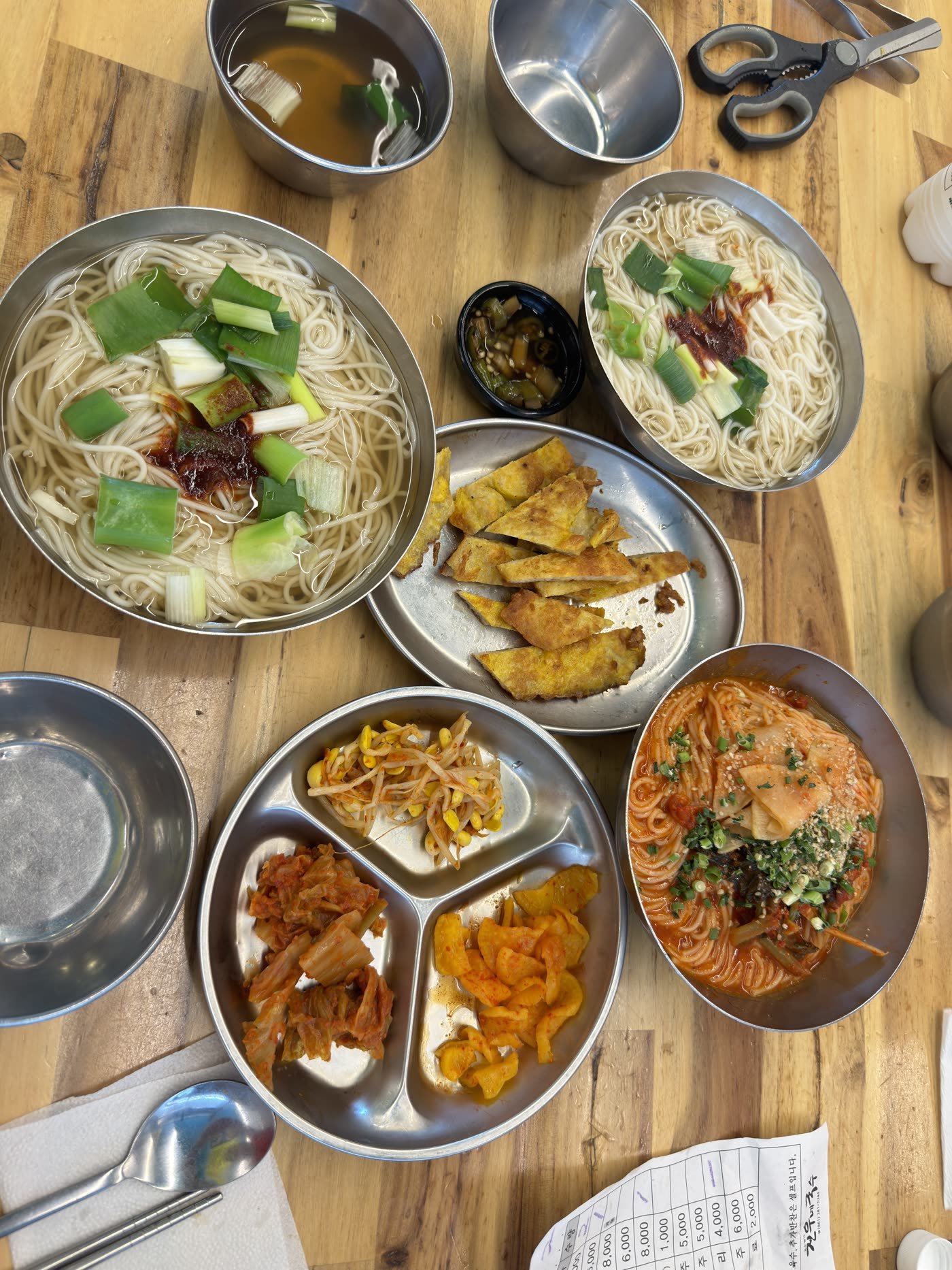 Bowls of janchi guksu, spicy noodles, jeon pancakes and side dishes in metal dishes at Damyang Guksu Street