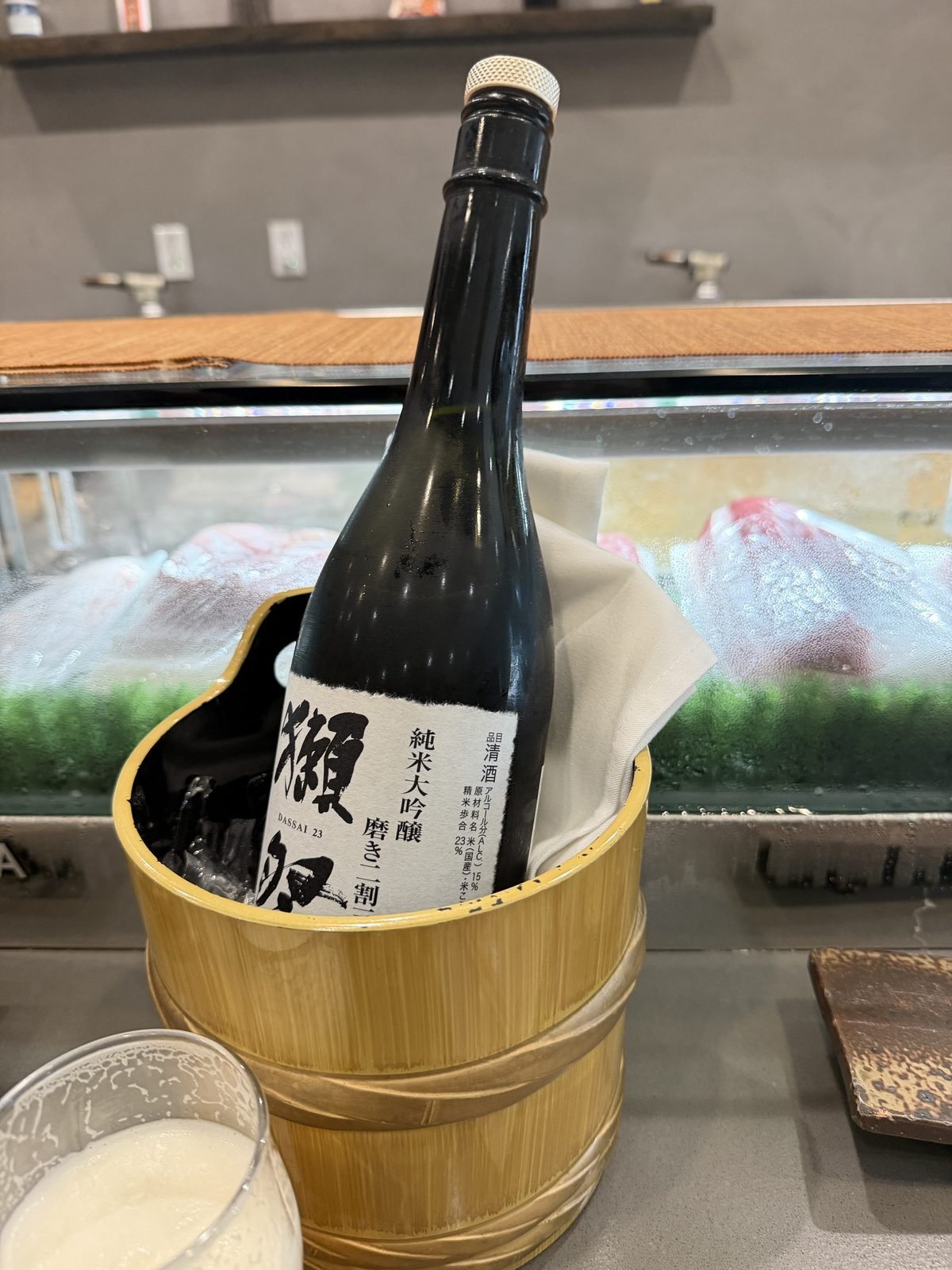 Bottle of Dassai junmai daiginjo sake chilling in a bamboo bucket at the sushi counter