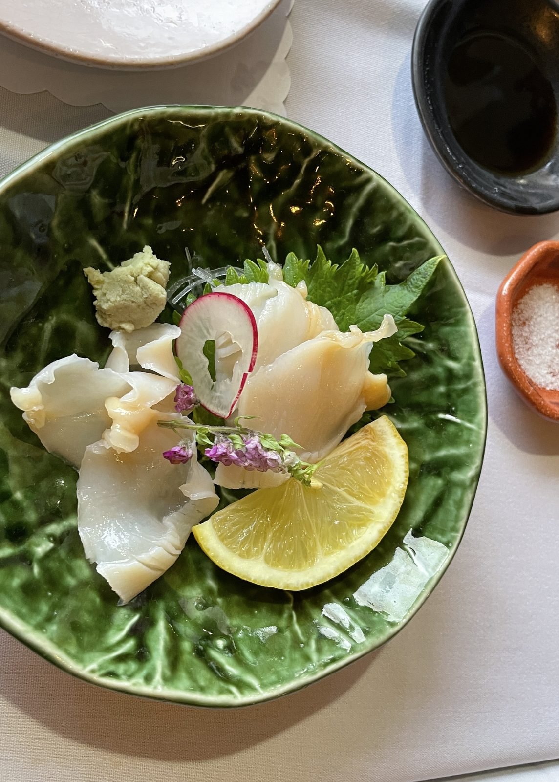 Jumbo clam sashimi with lemon and shiso on a green leaf plate at Matsumoto sushi