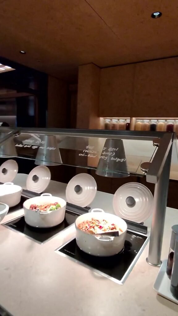 Covered pots of warm food on induction plates at the Korean Air lounge buffet in Incheon Terminal 2