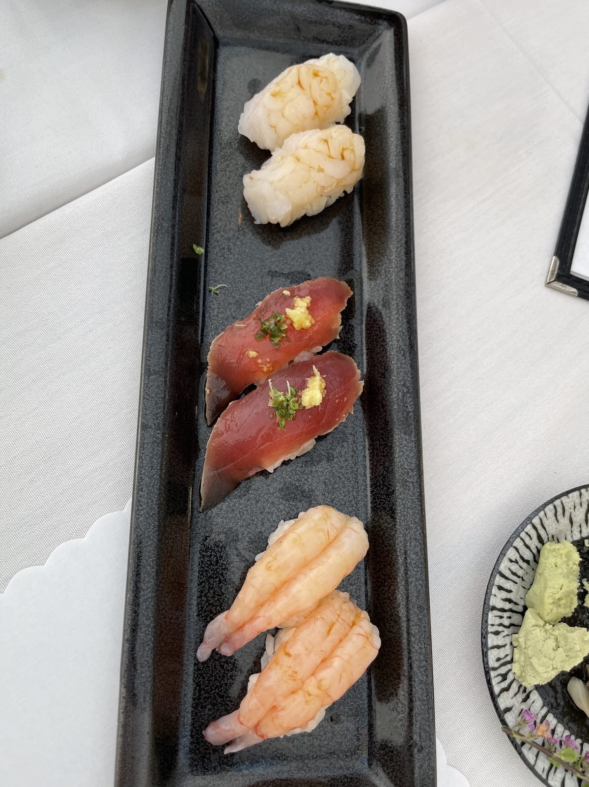 A flight of nigiri on a long black plate at Matsumoto sushi