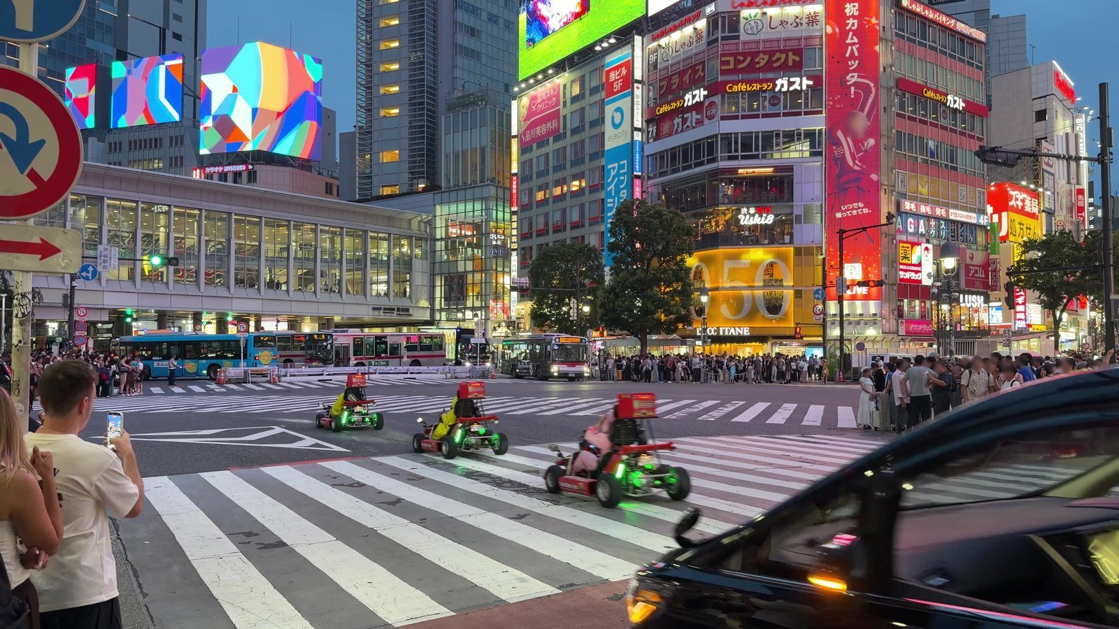 Neon signs above Shibuya Crossing as go-karts pass through