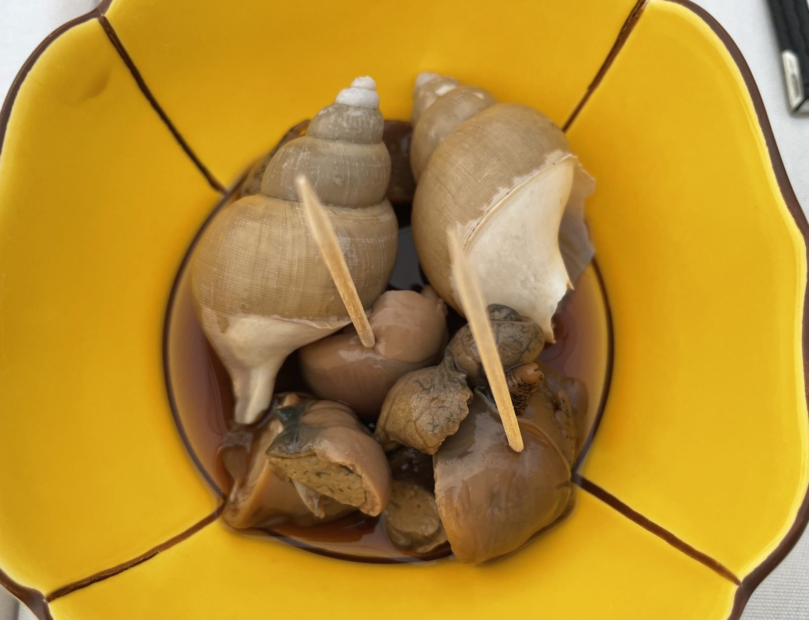 Simmered sea snails served with toothpicks on a yellow flower plate at Matsumoto sushi