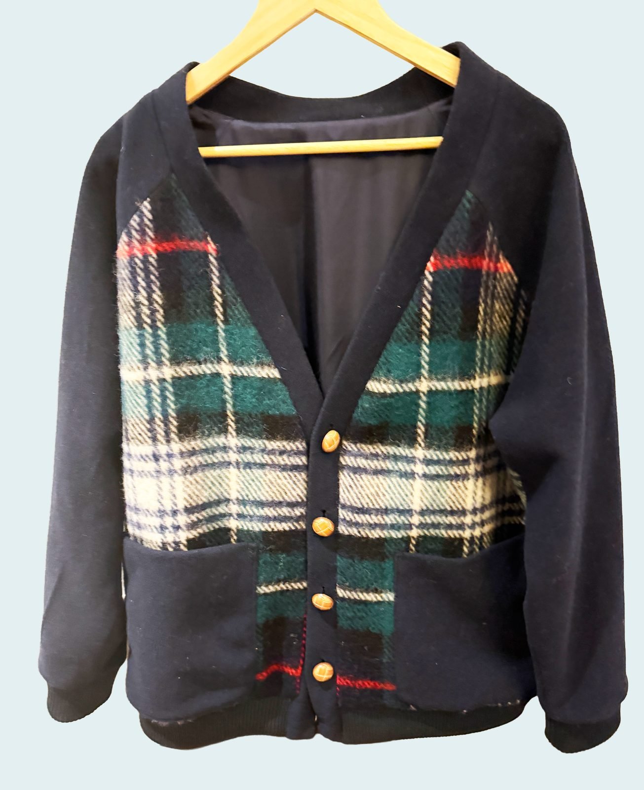 Handmade plaid wool cardigan with gold buttons on a hanger